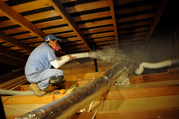 An energy doctor applying blown-in insulation to an attic space.