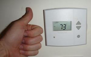 Person giving a thumbs up to their thermostat - set precisely at 73 degrees.